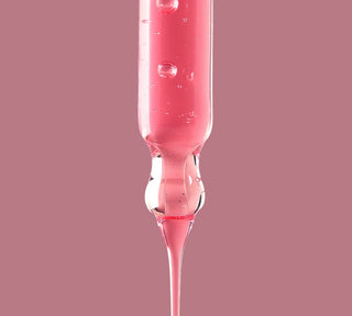 Un primo piano della texture lussuosa del siero viso ANUA, con il suo iconico colore rosa e consistenza leggera. La formula concentrata cattura la luce ed esalta l’effetto glow, sinonimo di pelle sana e idratata. L'immagine comunica purezza, innovazione e qualità premium del trattamento.